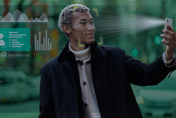 Pessoa segurando o celular em frente ao rosto enquanto o aparelho faz reconhecimento facial, com gráficos e informações pessoais sobrepostos representando coleta de dados por inteligência artificial.