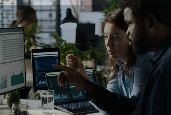 Dois analistas observam dashboards em monitores em um escritório moderno, representando a cultura de dados em pequenas e médias empresas.