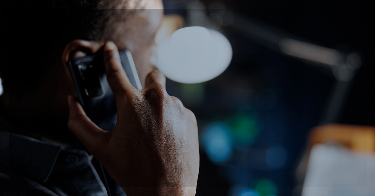 Pessoa ao telefone em ambiente escuro, ilustrando fraudes por telefone como spoofing e robocalls e a importância de proteger a operação